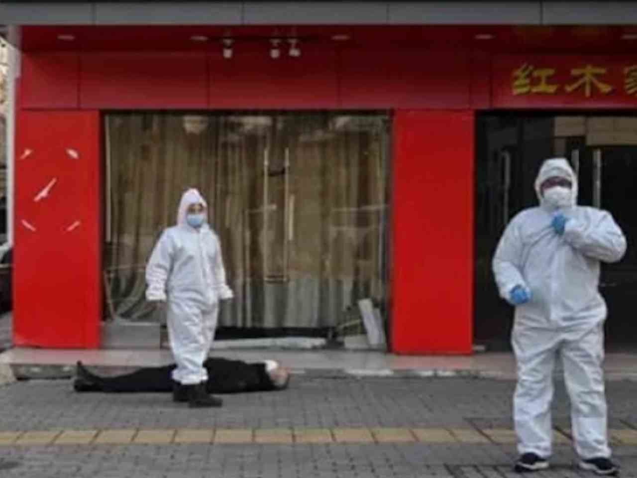 A body corps is lying in front of the restaurant in Wuhan behind the decontamination service workers on February 11, 2020.